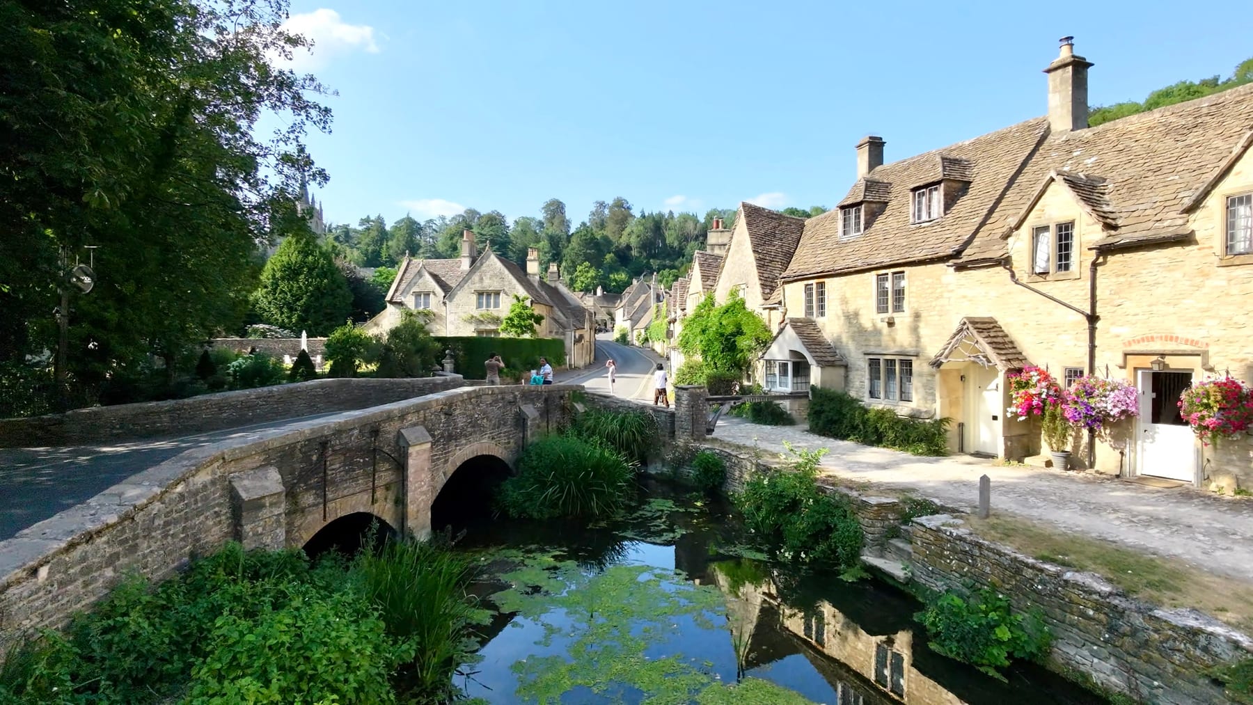 Vol bas au-dessus de Castle Combe en Angleterre, maisons de pierre, pont ancien et ruisseau au premier plan